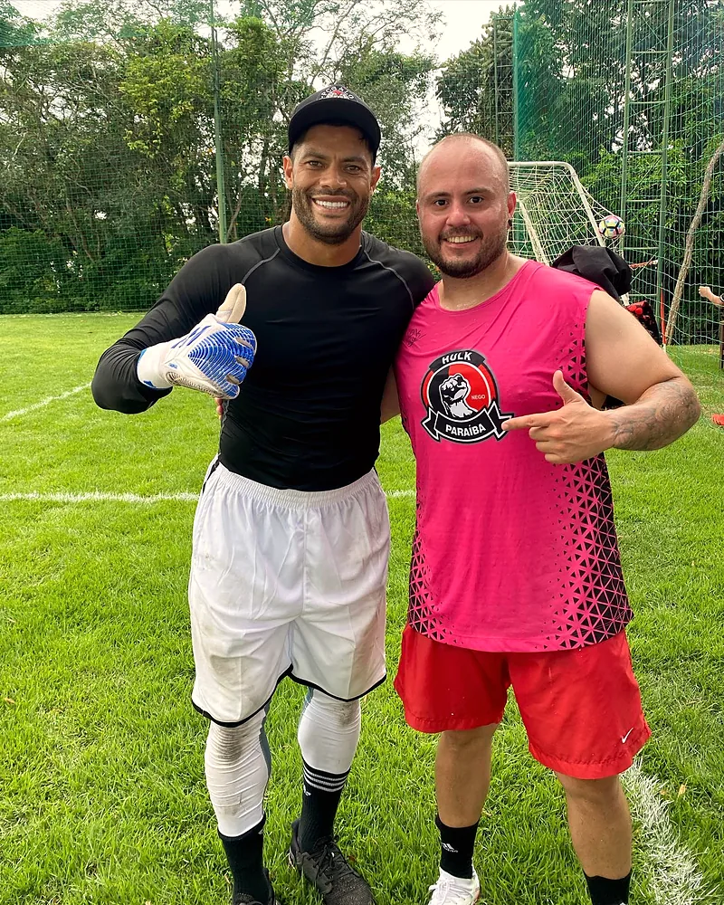 O Mateus de uniforme ao lado de Hulk, num campo de futebol